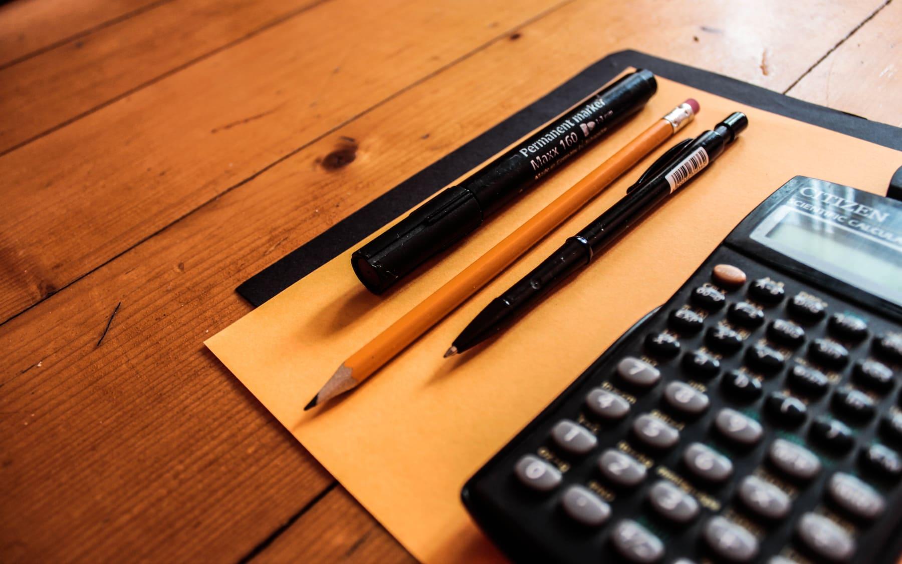Calculatrice, stylos et crayon posés sur un bureau pour réviser