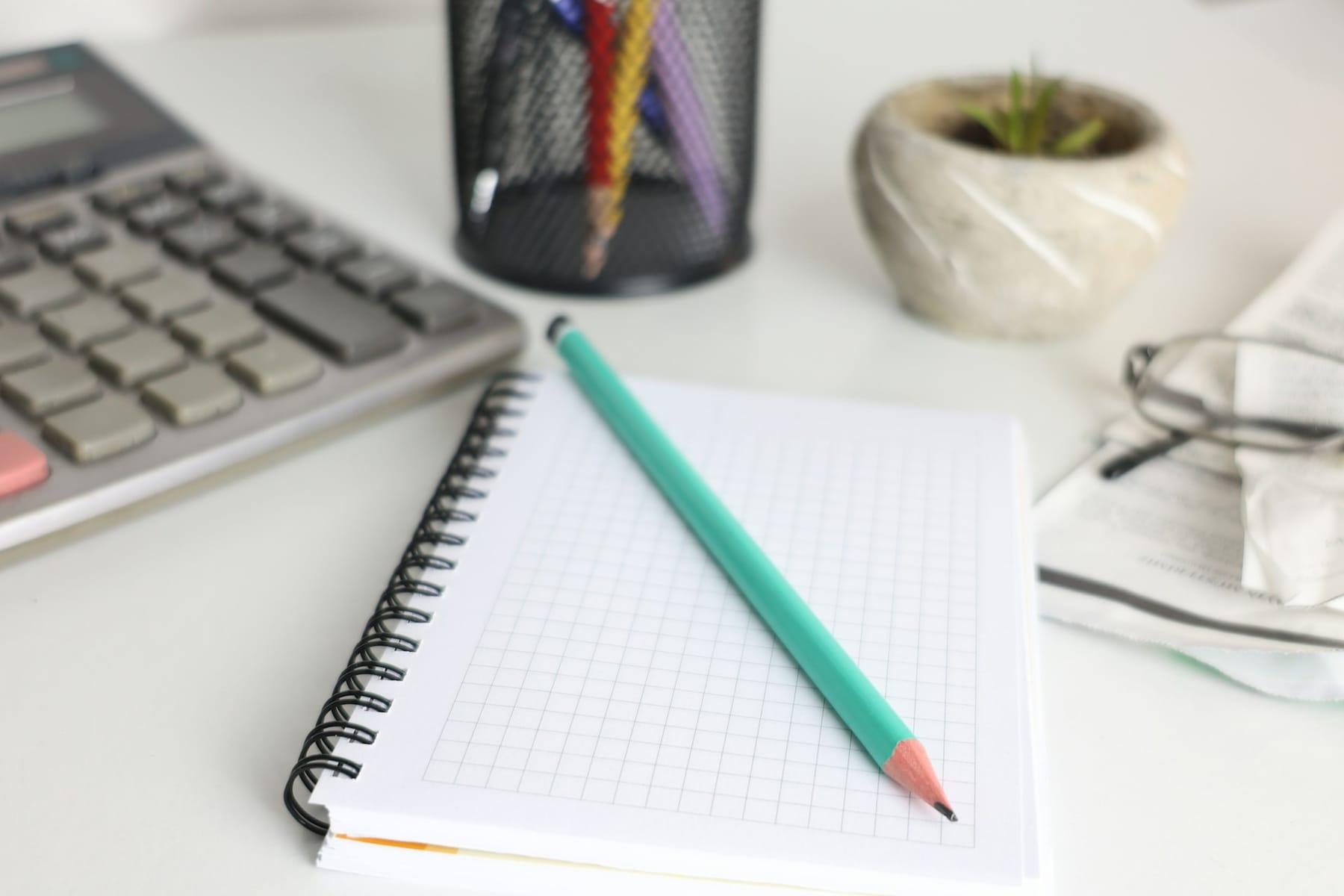 Un cahier à petits carreaux, un crayon et une calculatrice posés sur un bureau